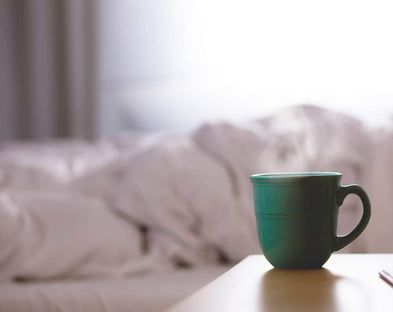 Mug of coffee next to cozy bed
