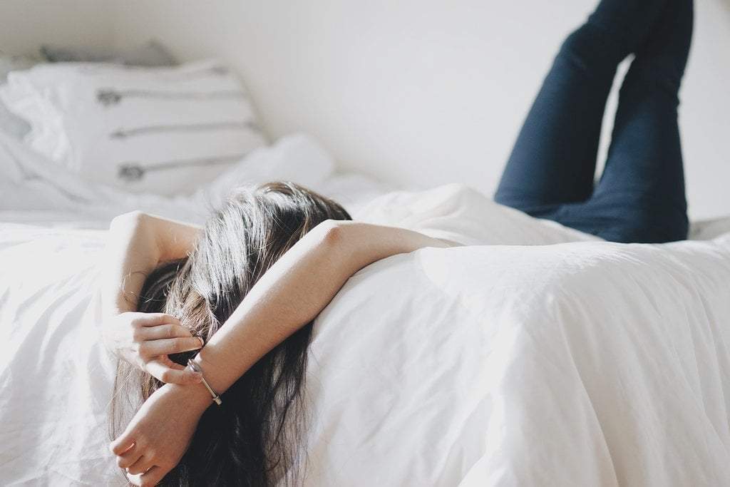 A woman lounges in her clean bed sheets.