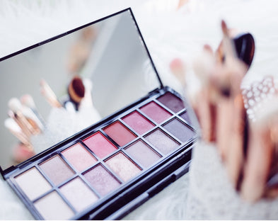 Eyeshadow and makeup brushes sit on a bed.