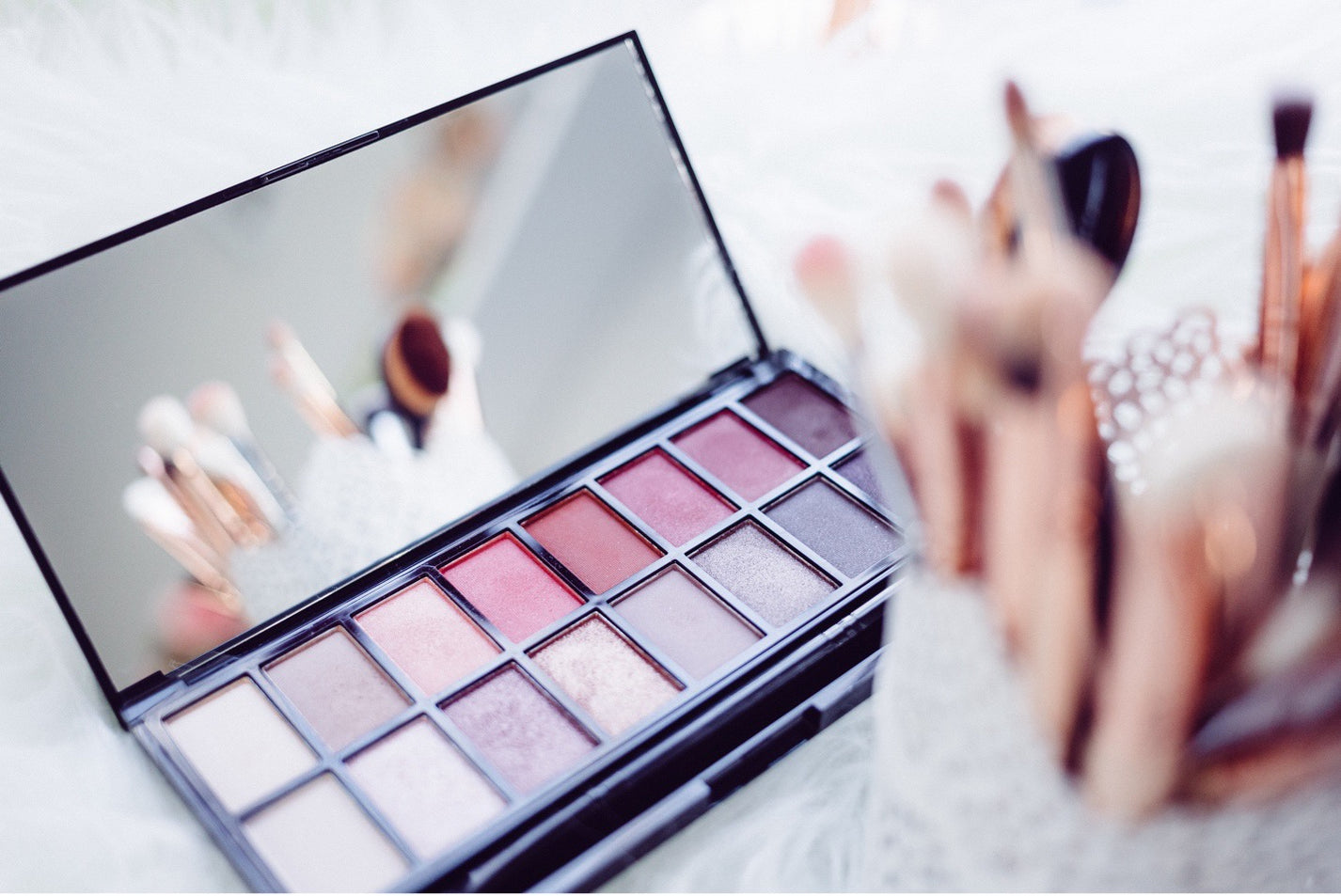 Eyeshadow and makeup brushes sit on a bed.