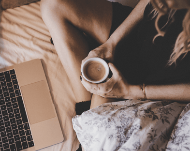 Woman with laptop and coffee cozy in bed