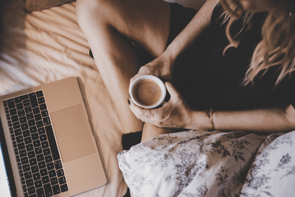 Woman with laptop and coffee cozy in bed