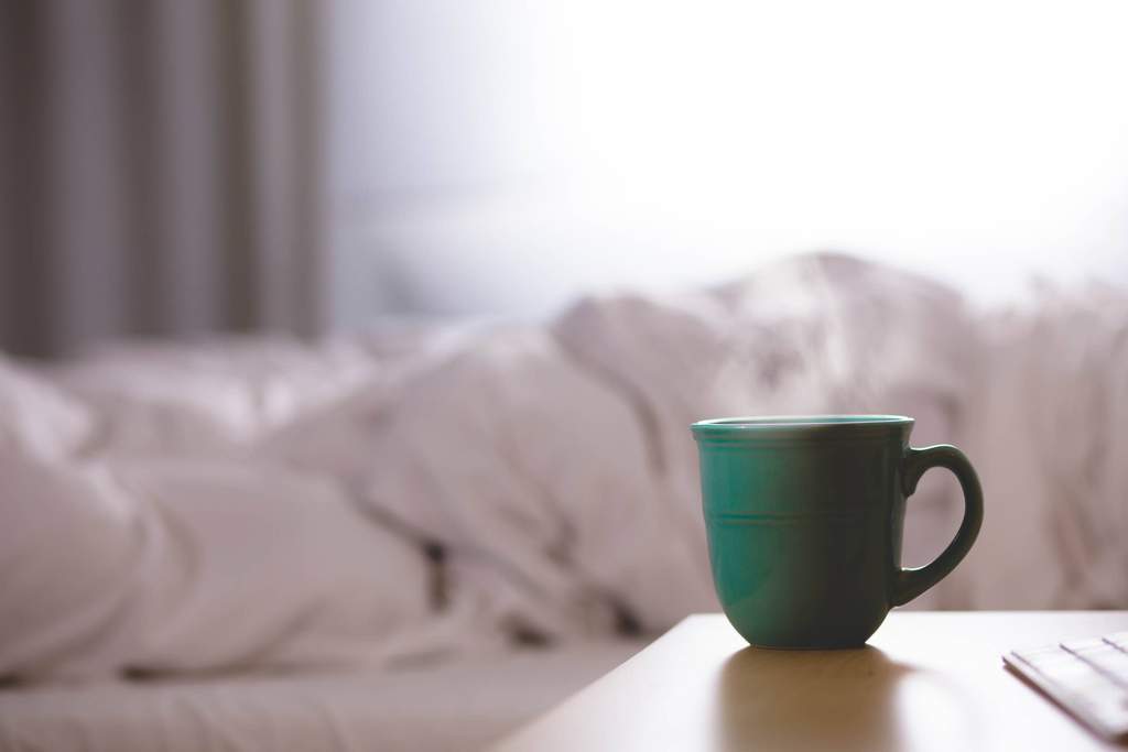 Mug of coffee next to cozy bed